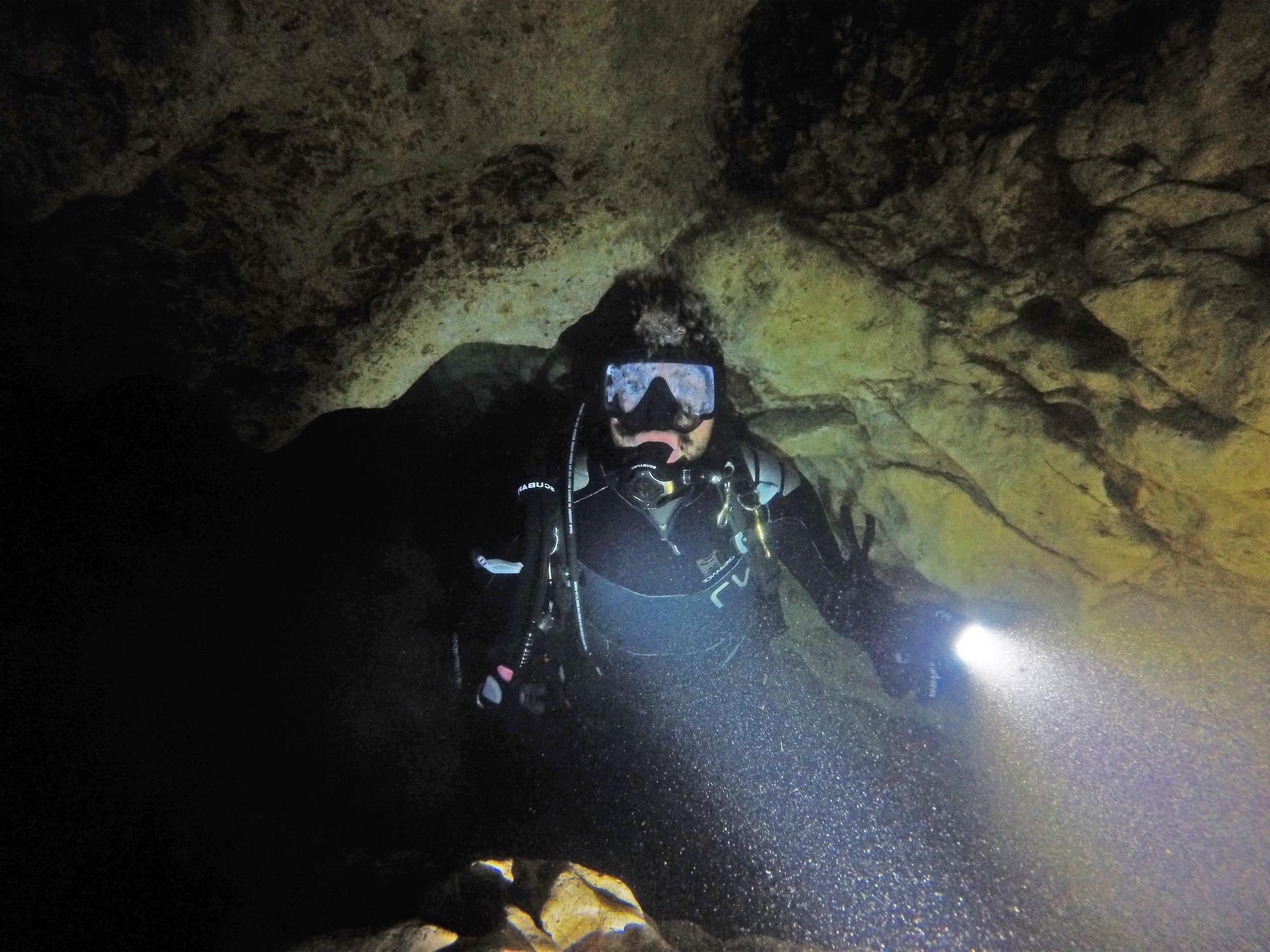 一个人穿着全套潜水装备在黑暗的洞穴里潜水. 